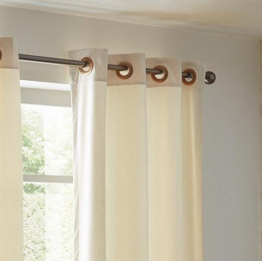White curtains with wooden rings on a rod against a neutral wall.