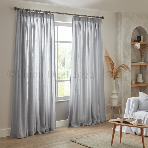 Gray curtains hanging in a room with a window, sofa, and small table.