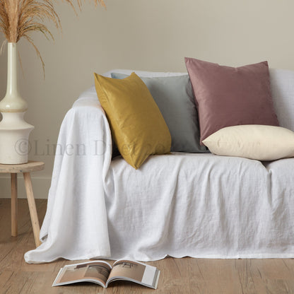 White sofa with colorful pillows and an open magazine on a wooden floor.