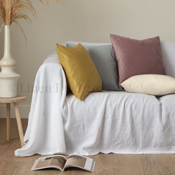 White sofa with colorful pillows and an open magazine on a wooden floor.