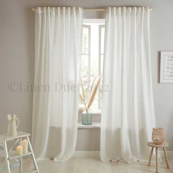 White linen curtains in a room with a small table and decor items.