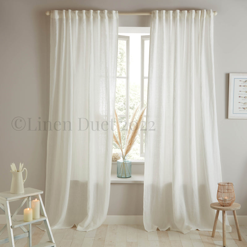 White linen curtains in a room with a small table and decor items.