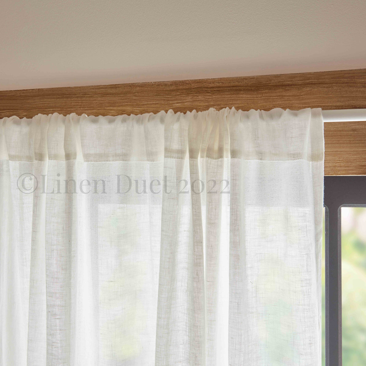 White linen curtain with a wooden rod and blurred outdoor background