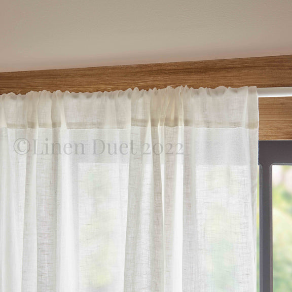 White linen curtain with a wooden rod and blurred outdoor background