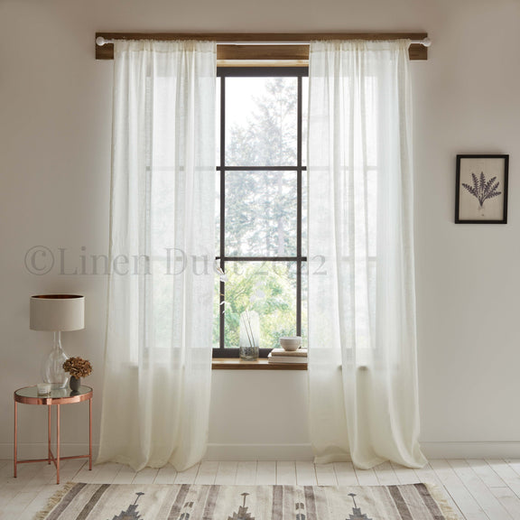 Sheer white curtains hanging in a room with a lamp and small table.