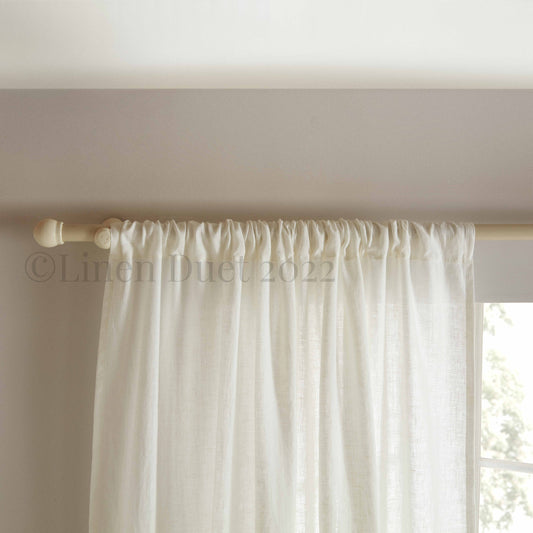 White curtain panel with a wooden rod on a neutral background
