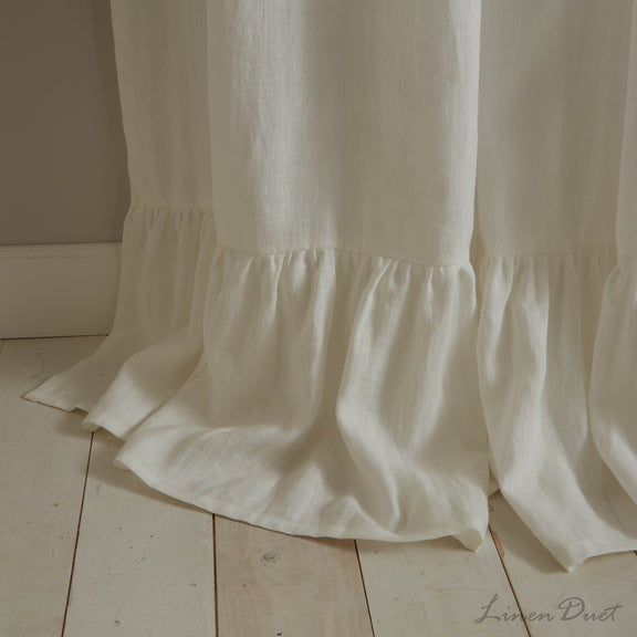 White curtain with ruffled bottom edge on a wooden floor.