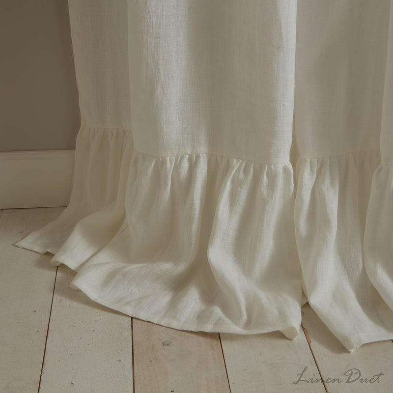 White curtain with ruffled bottom edge on a wooden floor.