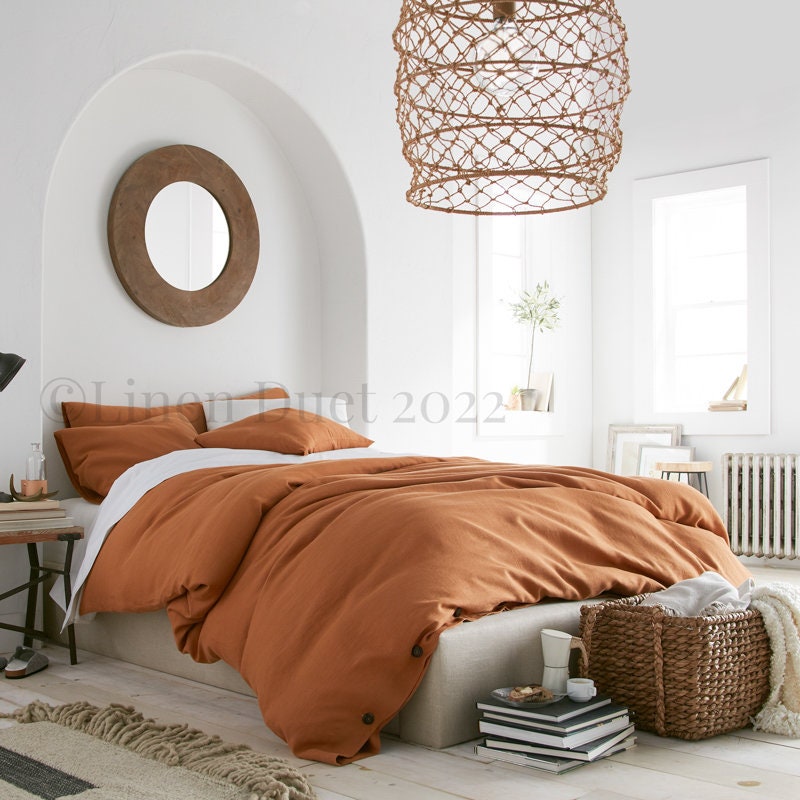 Cozy bedroom with orange bedding and a woven pendant light.
