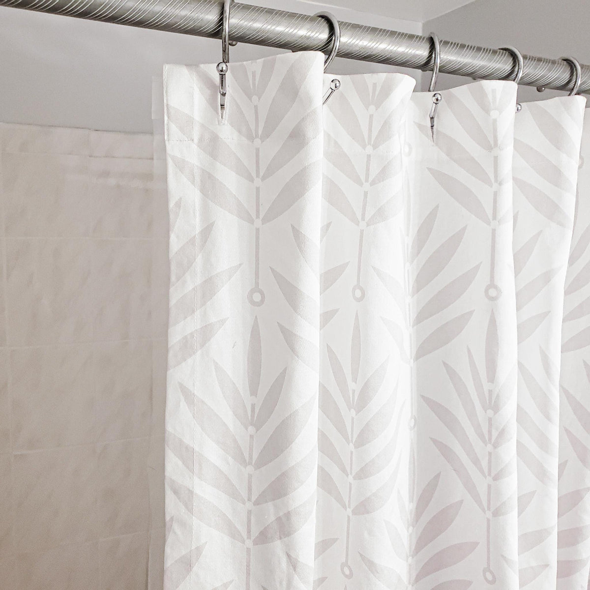 White shower curtain with leaf pattern hanging on a silver curtain rod.
