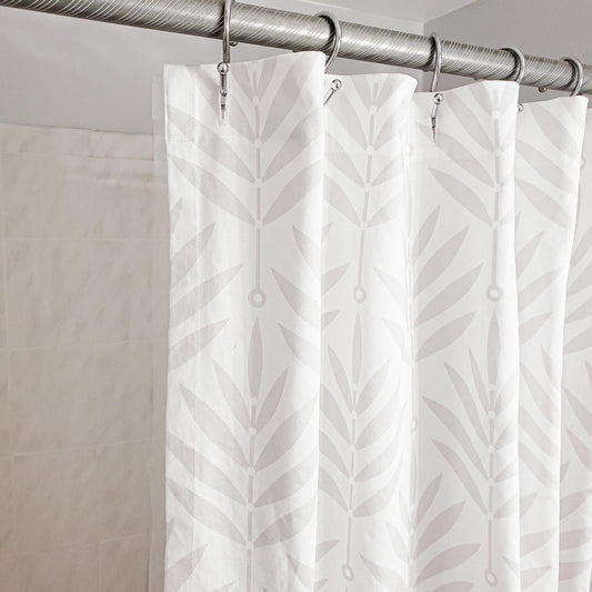 White shower curtain with leaf pattern hanging on a silver curtain rod.