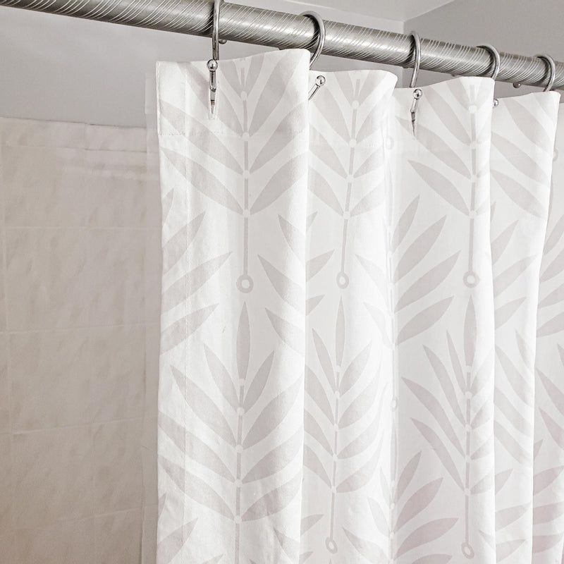 White shower curtain with leaf pattern hanging on a silver curtain rod.