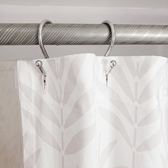 Curtain with leaf pattern hanging on a silver curtain rod against a neutral background
