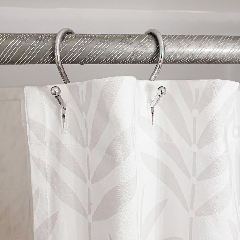 Curtain with leaf pattern hanging on a silver curtain rod against a neutral background