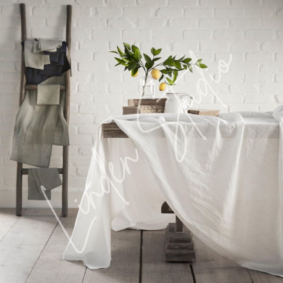 White tablecloth draped over a table with a plant and books against a white brick wall.