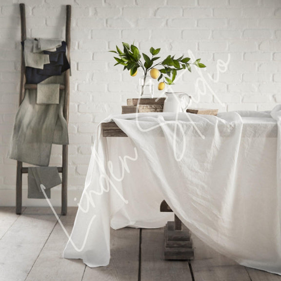 White tablecloth draped over a table with a plant and books against a white brick wall.