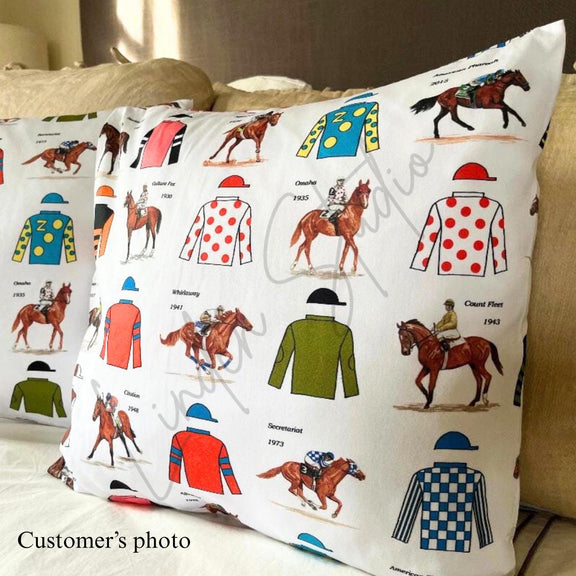 Decorative pillow with horse racing-themed design featuring jockeys and horses on a white background.