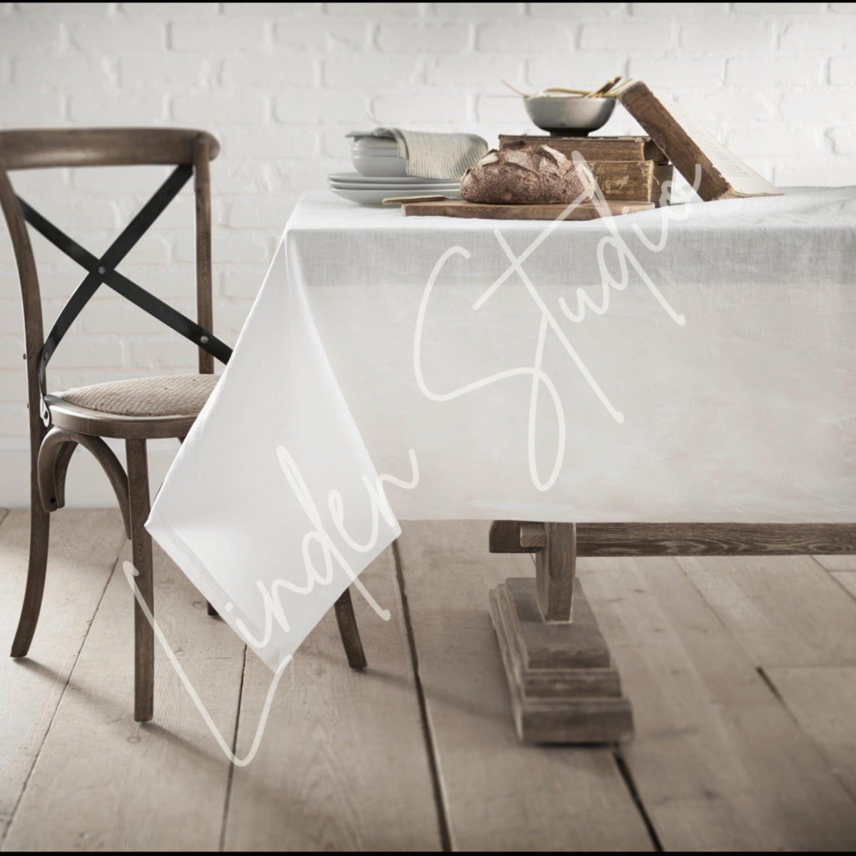 Dining table with a white tablecloth featuring 'Under Study' text, wooden chair, and rustic decor.
