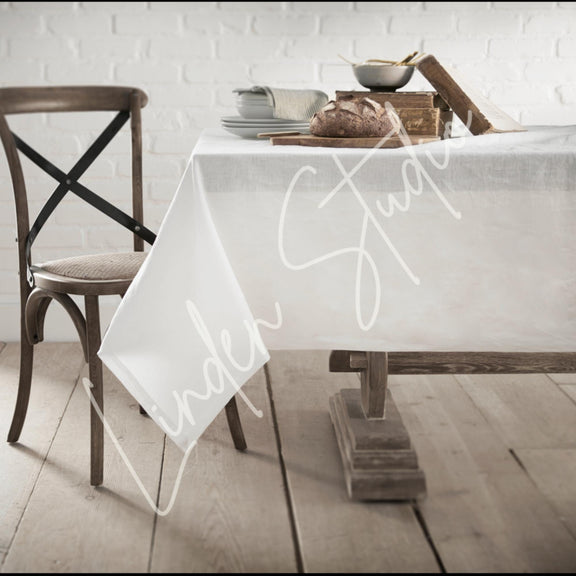 Dining table with a white tablecloth featuring 'Under Study' text, wooden chair, and rustic decor.