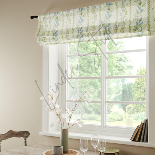 Window with green and white patterned roman blind, light streaming through, and a vase with flowers on a windowsill.