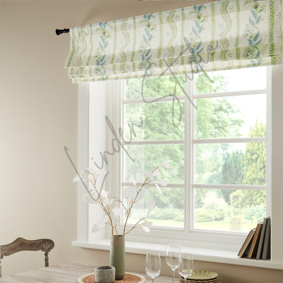 Window with green and white patterned roman blind, light streaming through, and a vase with flowers on a windowsill.