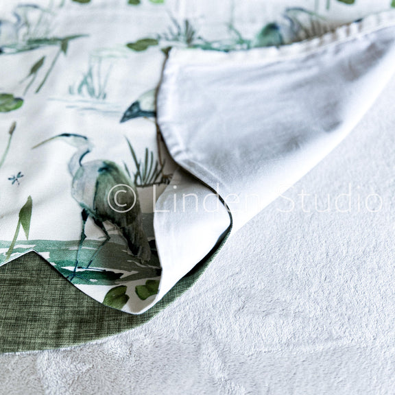 Close-up of a fabric with a nature-themed pattern and white border.