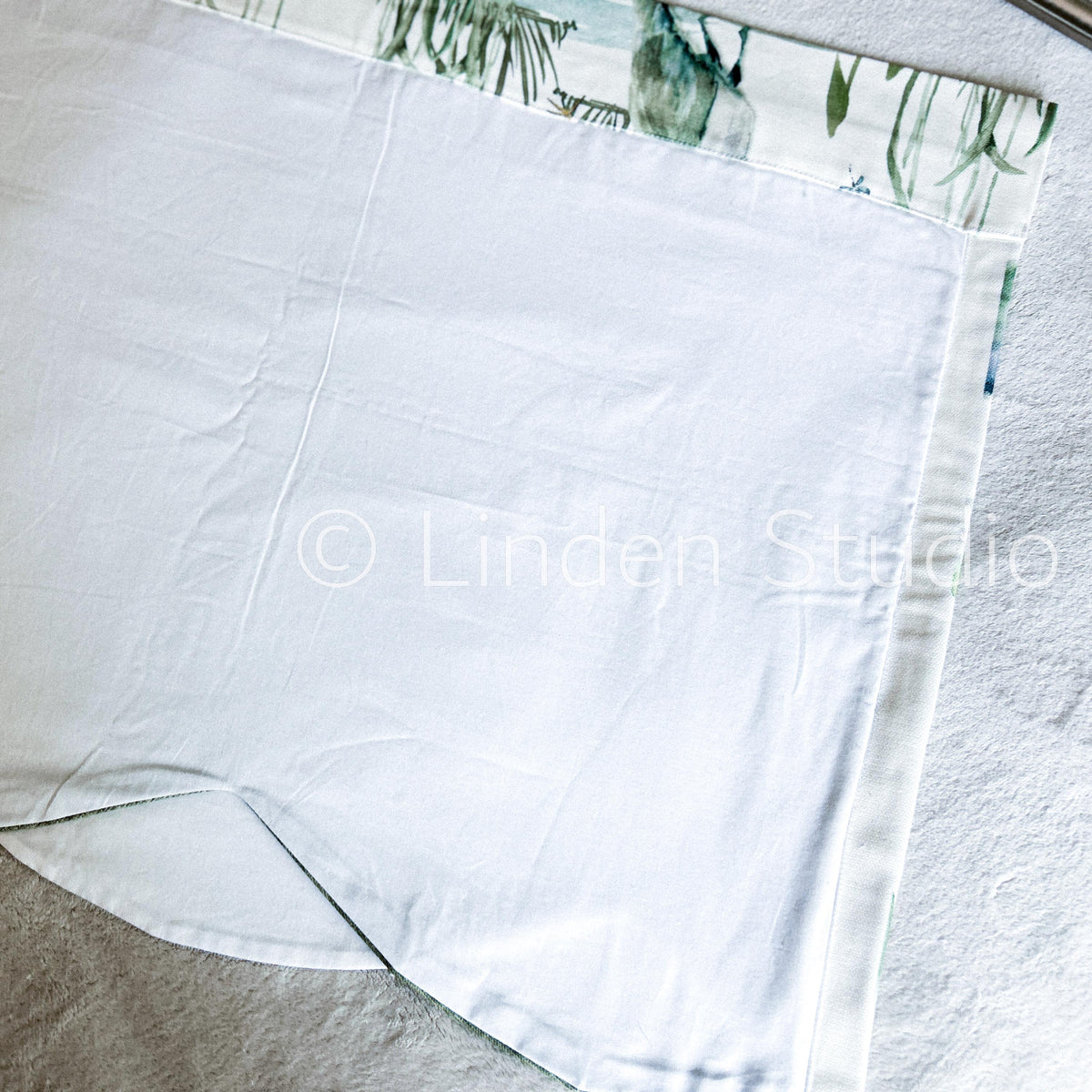 White fabric with a green leaf pattern at the top corner on a light gray background.