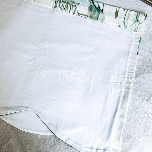 White fabric with a green leaf pattern at the top corner on a light gray background.