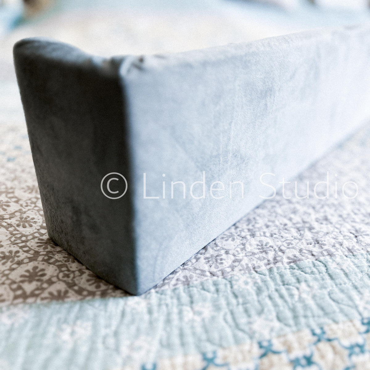 Gray wedge pillow on a patterned bedspread with 'Linden Studio' watermark.