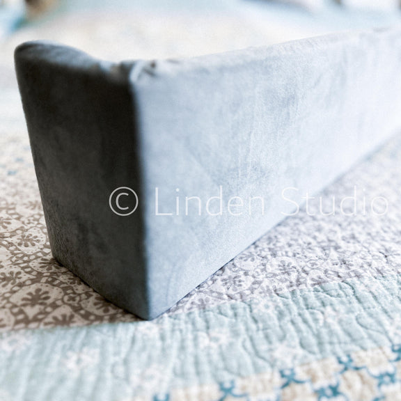 Gray wedge pillow on a patterned bedspread with 'Linden Studio' watermark.