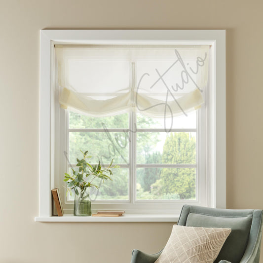 Window with white frame and sheer curtain, view of greenery outside, beige wall and gray chair.