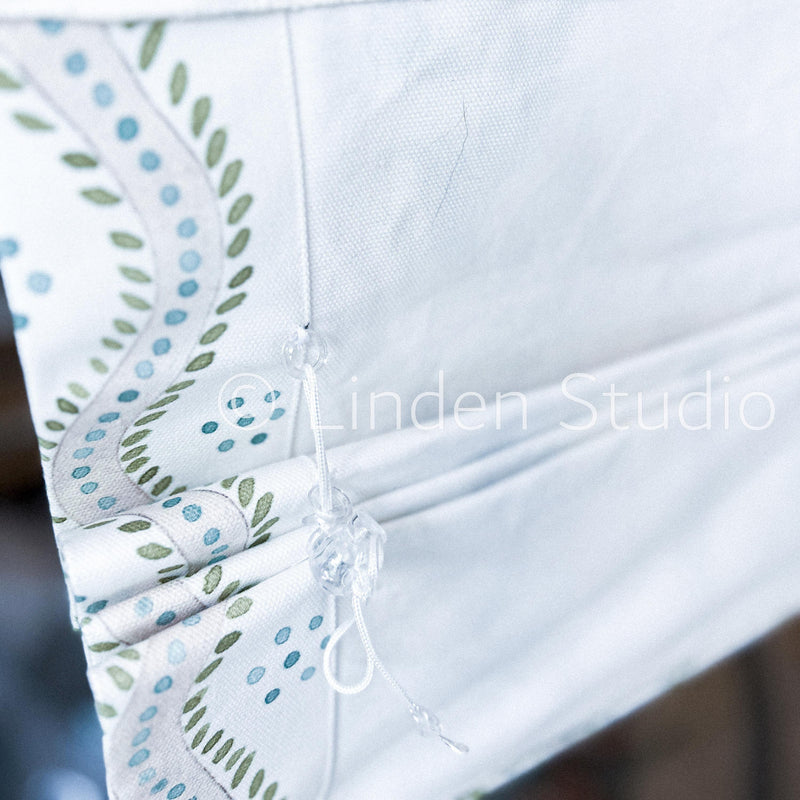 Close-up of a white garment with green and blue floral embroidery, featuring 'Linden Studio' branding.